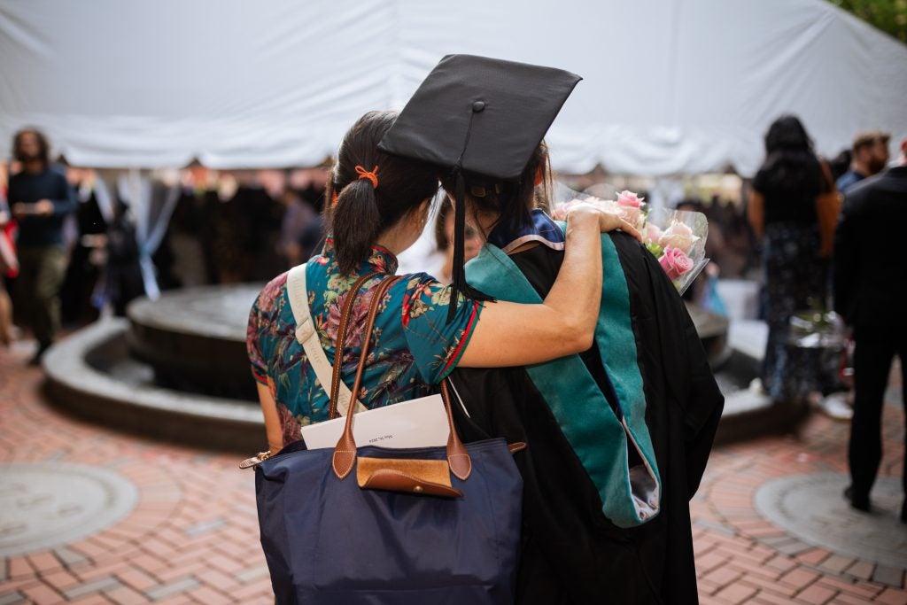 A commencement attendee wraps her arm around a graduate's back.