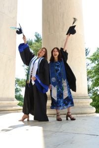A mother and daughter lift their caps in the air as they wear their graduation gowns.