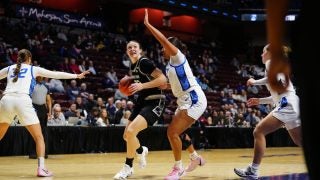 A women&#039;s basketball player dribbles toward the basket as her opponent attempts to block her on the court.