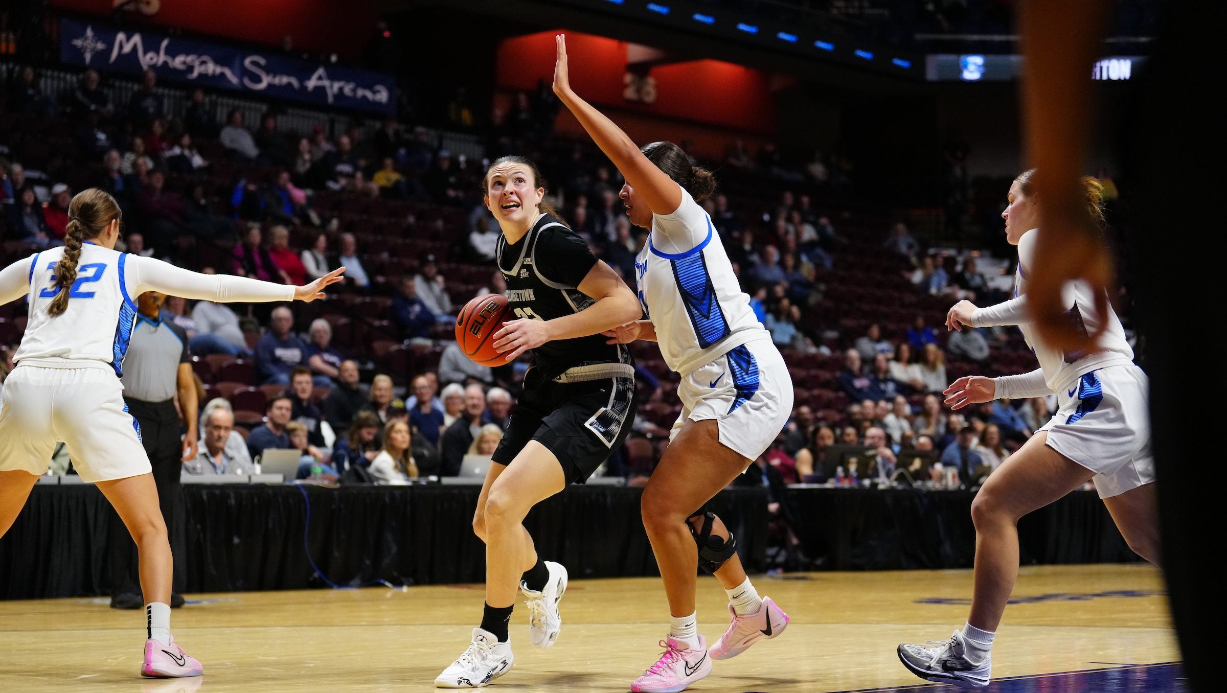 A women's basketball player dribbles toward the basket as her opponent attempts to block her on the court.