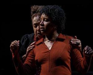 A Black woman guides another Black woman in her movements for a musical.