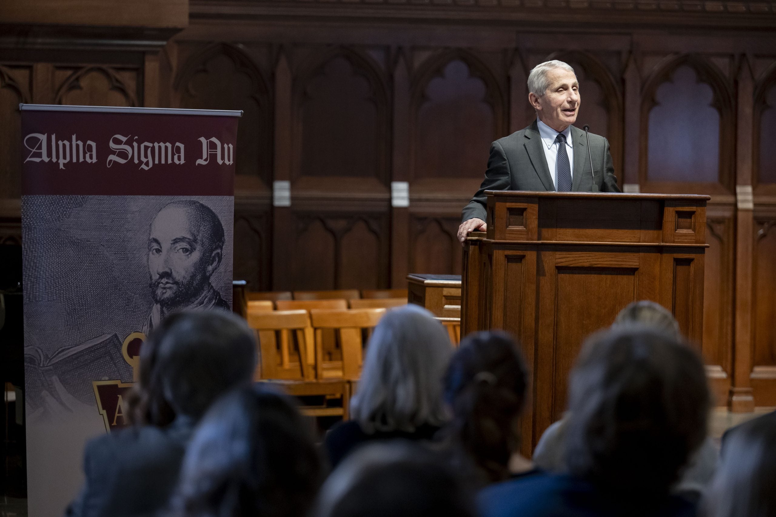 Dr. Fauci in Dahlgren chapel speaking at the podium with an Alpha Sigma Nu pop up banner next to him.
