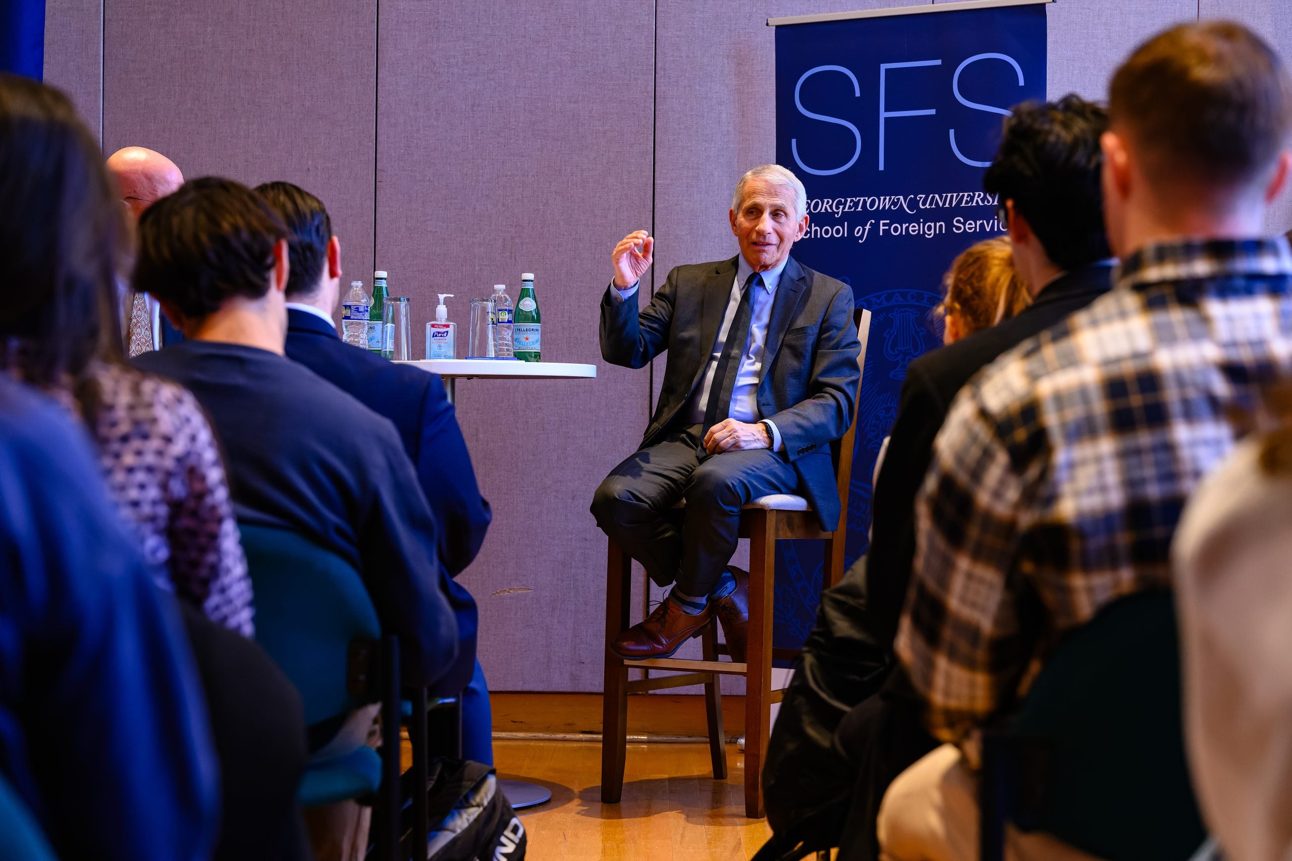Fauci sitting in a chair at a SFS event talking to a room of students.
