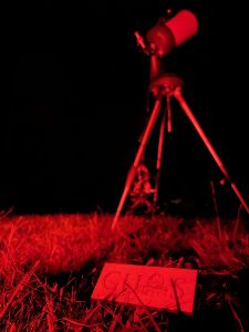 A telescope with a paper promoting the astronomy club illuminated by red light