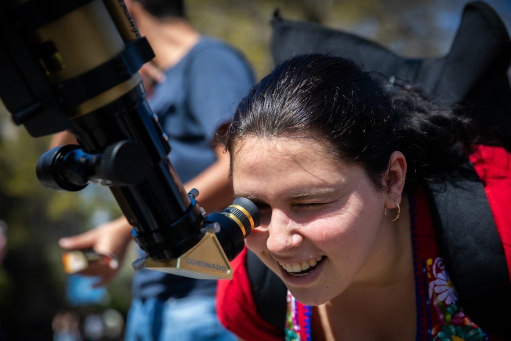 Young woman looking through a telescope on a sunny day