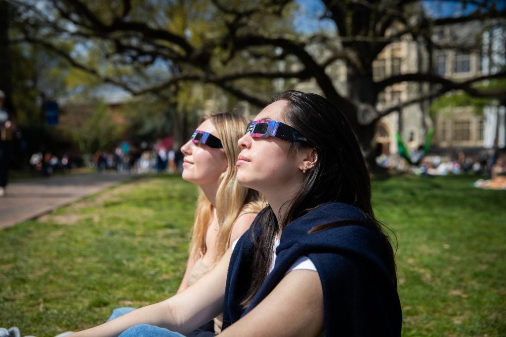 Two young women on Healy Lawn looking at the eclipse with eclipese glasses