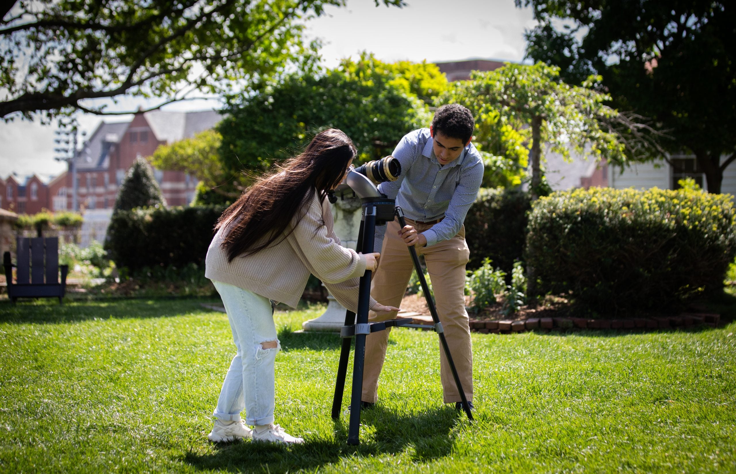 Two students set up a telescope in a green lawn.