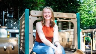 Liz Fortier sitting on a playground slide wearing jeans and an orange tank top
