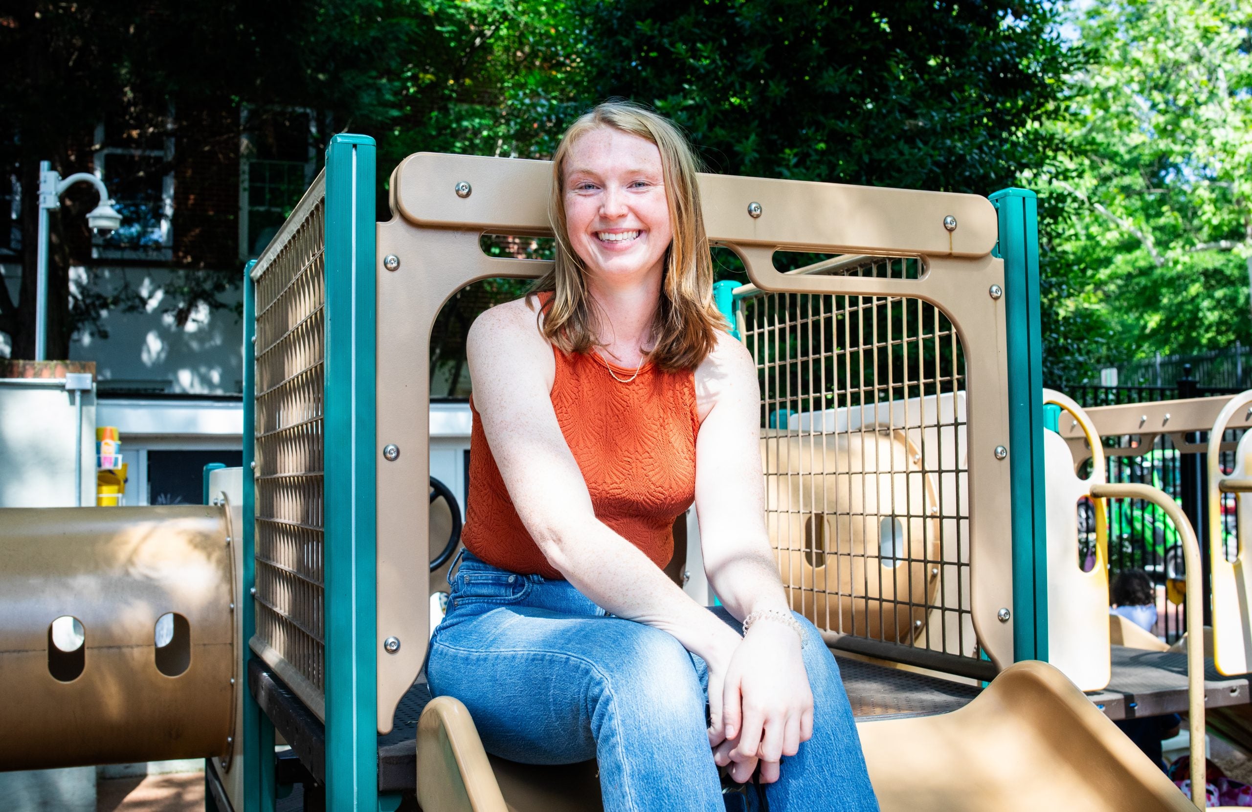 Liz Fortier sitting on a playground slide wearing jeans and an orange tank top