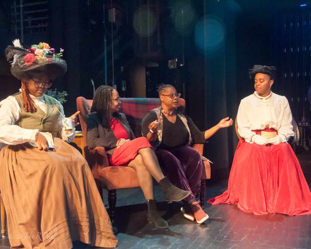 Four women on a stage. Two are wearing costumes for a play.