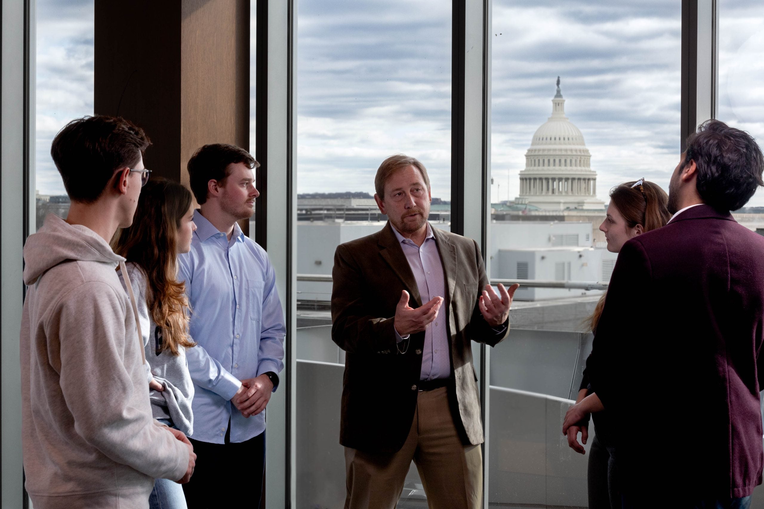A professor talking to five students with a view of the Capitol in the background.