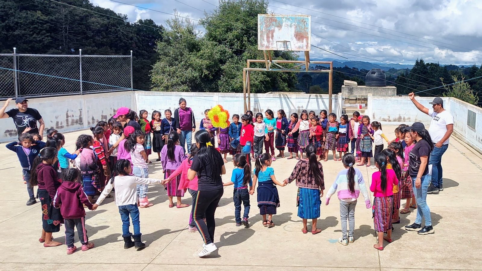 Teachers holding hands with a group of children, forming a circle and playing together outdoors.
