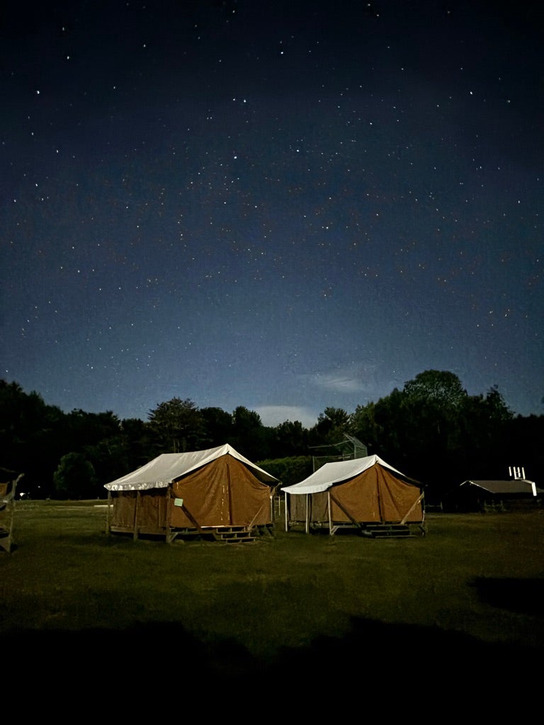 Two tents on a field at night with stars shining brightly