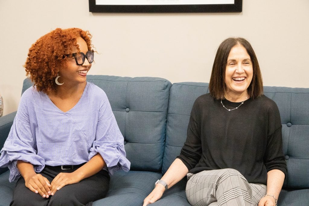 Two women sit side-by-side on a blue couch