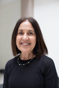 A woman with brown hair wearing a black sweater smiles.