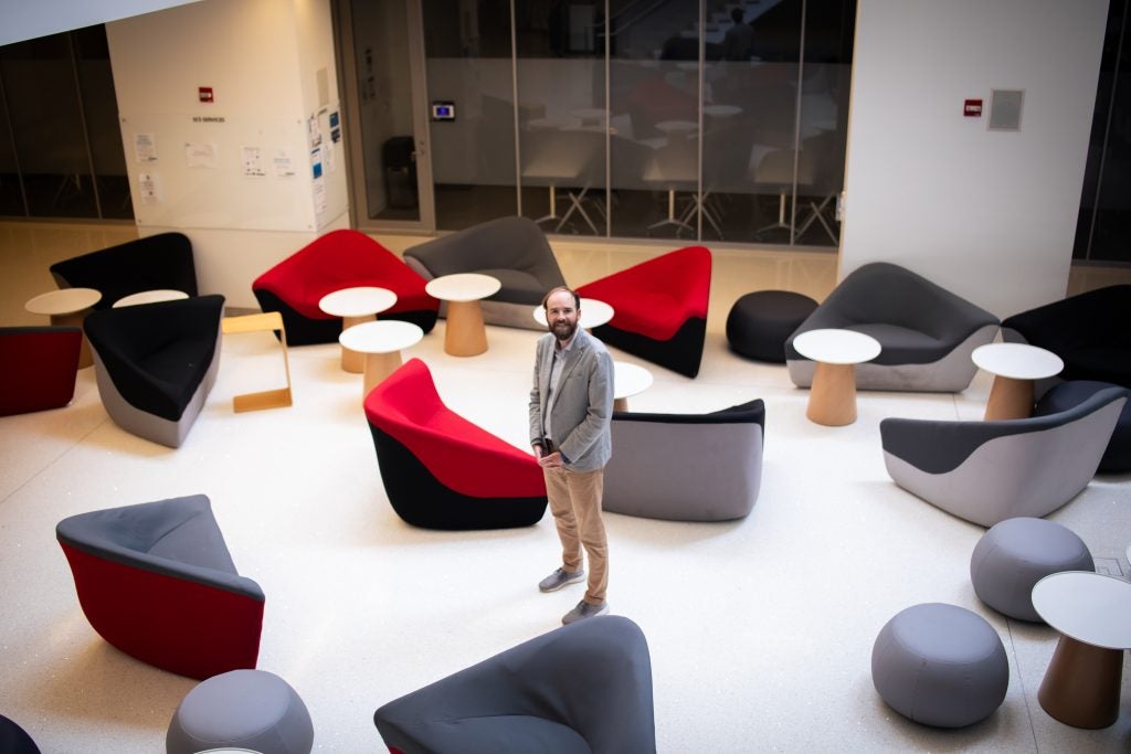 A man stands in the middle of a study area filled with modern chairs and tables.