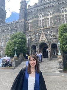 Neval Mulaomerovic at her graduation from Georgetown in 2024. She wears a black graduation gown and smiles in front of a stone building.