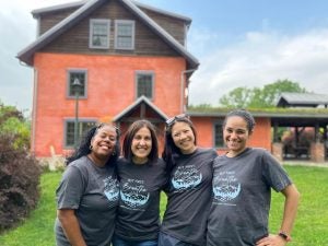 A group of women in gray T-shirts stand in front of a red brick building.