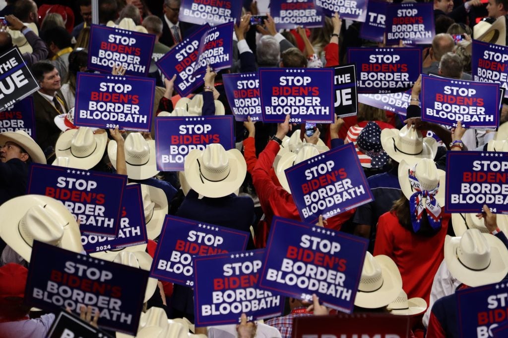 People in cowboy hats holding up campaign signs saying "Stop Biden's Border Bloodbath"