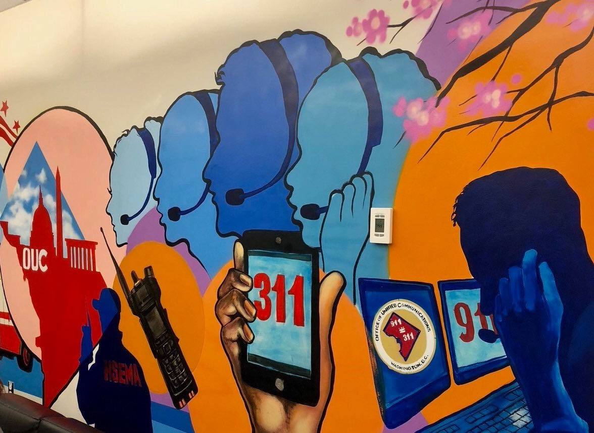 A bright orange and blue mural of silhouettes of faces with a headset on and a hand holding up a phone that says "311" on the screen.