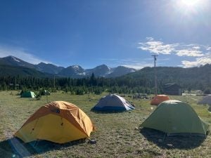 Tents pitched on a field with the Rockies in the background on a sunny day