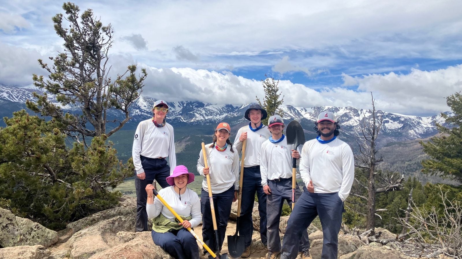Six people in white shirts standing on top of a mountain on a cloudy day