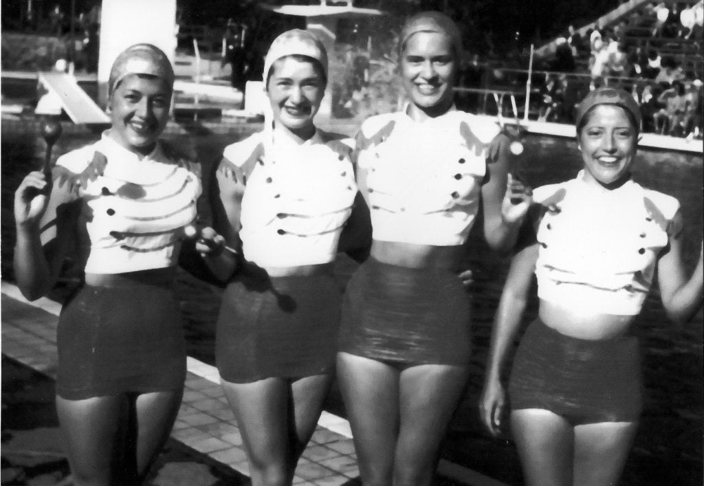 A black-and-white photo of four women in swimming outfits and swimcaps similing for a picture together in 1952.