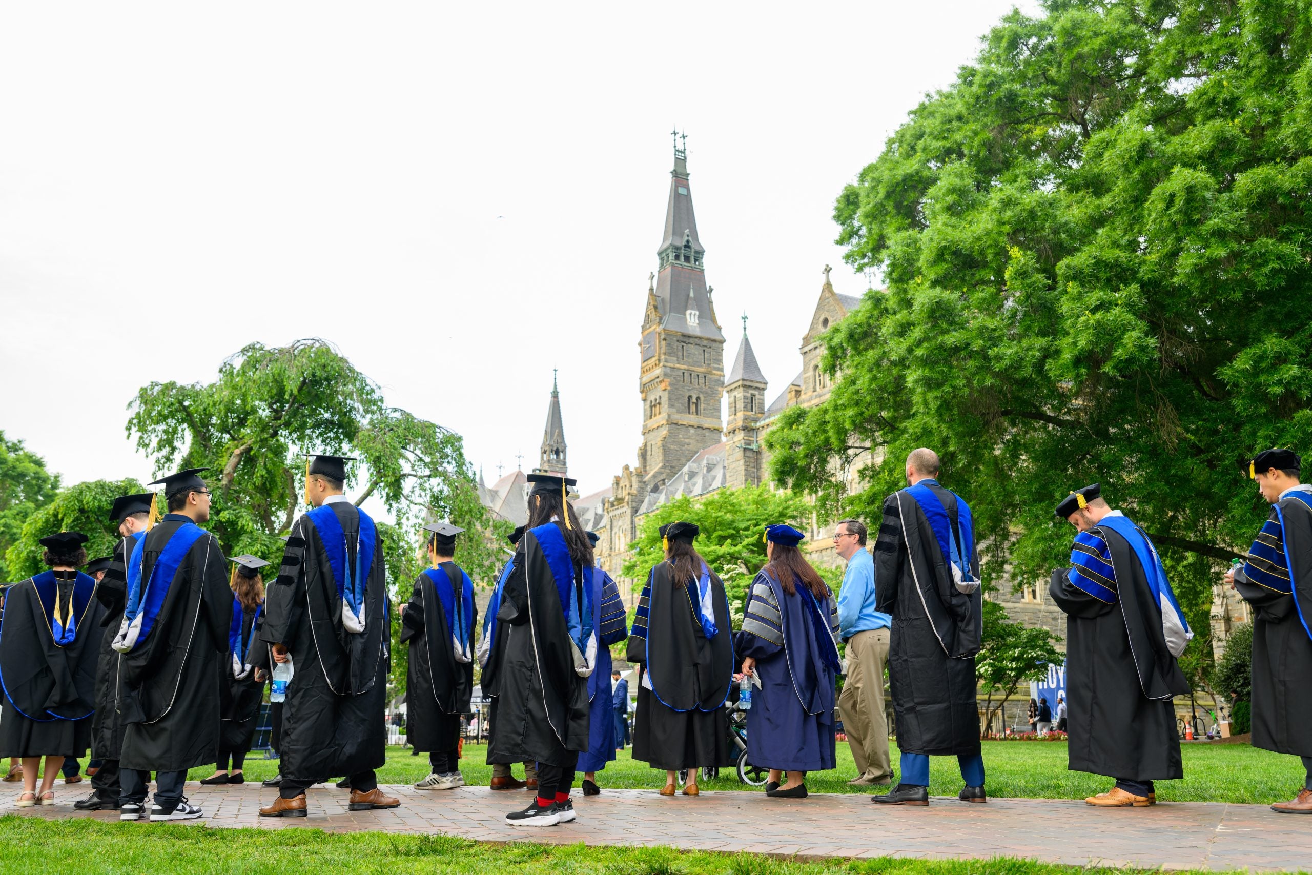 A group of people in graduation caps and gowns look up at the Georgetown clocktower.