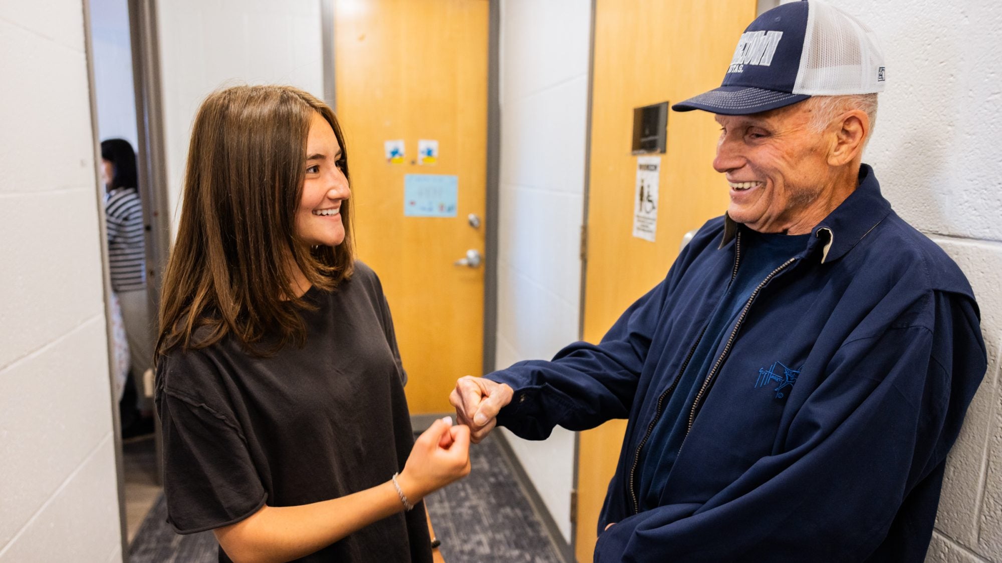 A granddaughter and grandfather fist-pump in a dorm hallway.