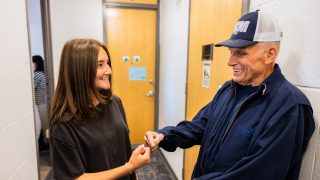 A granddaughter and grandfather fist-pump in a dorm hallway.