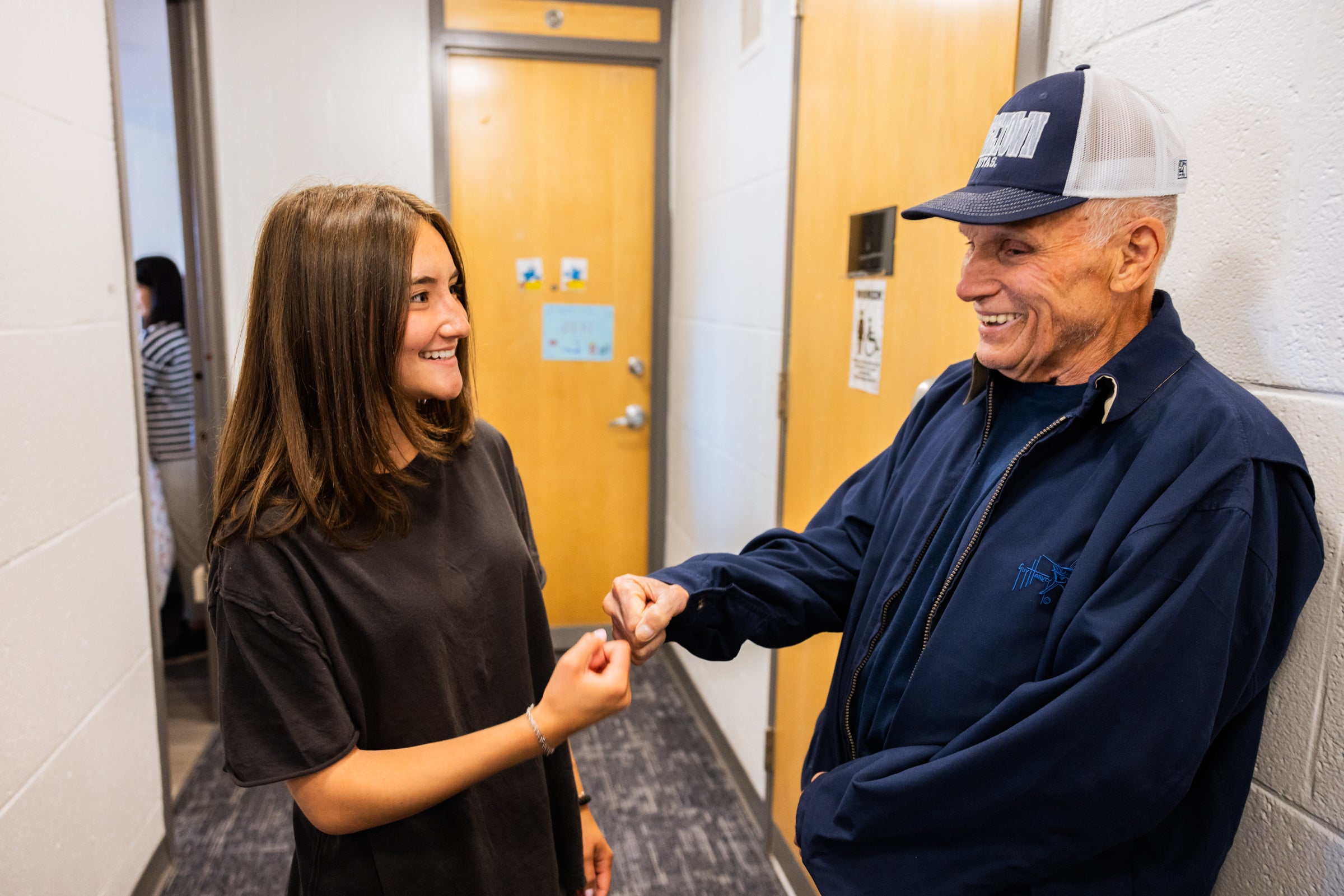 A granddaughter and grandfather fist-pump in a dorm hallway.