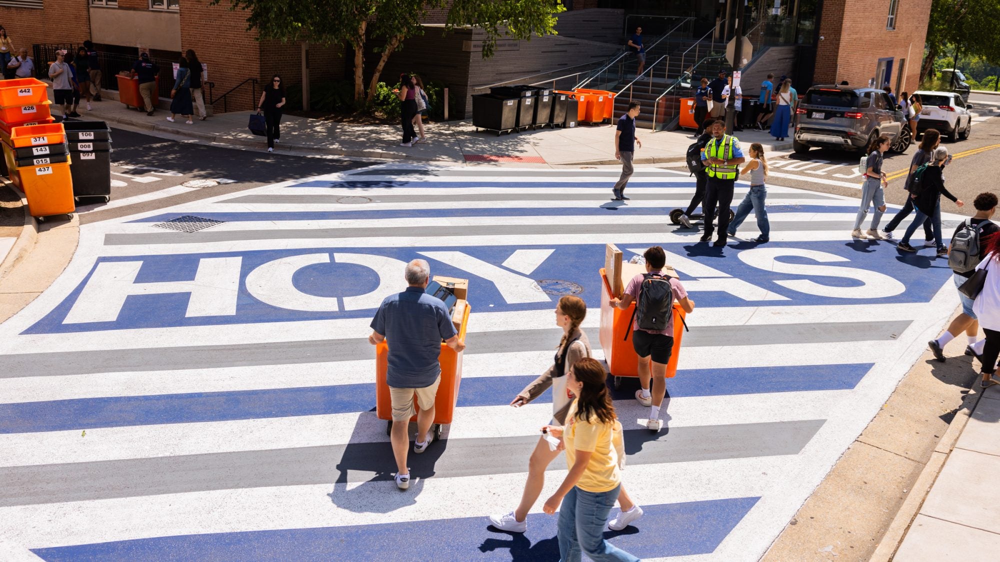 Parents and students with moving bins going across the street with &quot;Hoyas&quot; printed on the road