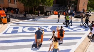 Parents and students with moving bins going across the street with &quot;Hoyas&quot; printed on the road