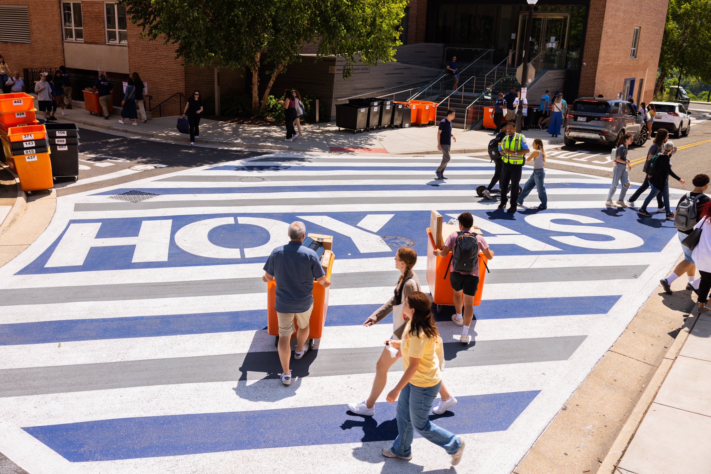 Parents and students with moving bins going across the street with "Hoyas" printed on the road