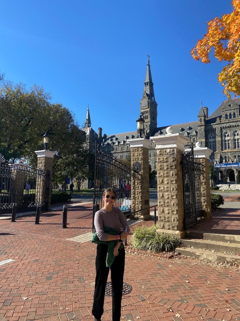 A young woman stands in front of Georgetown's clocktower on a bright sunny day.