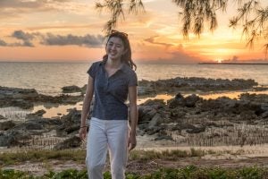 A college student smiles in front of a beach sunset.