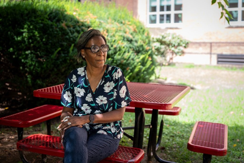 A woman sits at an outdoor picnic table on green grass.