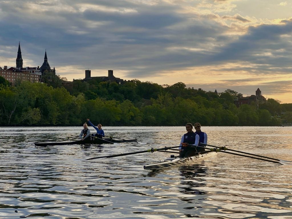 Four people in two separate boats rowing with Healy Hall in the background in the morning