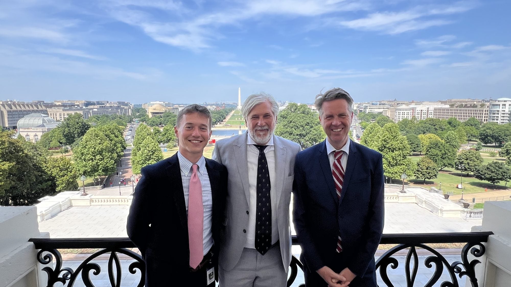 Hughes standing with two men all in suit and ties on the speaker&#039;s balcony overlooking the National Mall