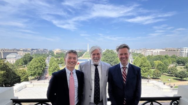 Hughes standing with two men all in suit and ties on the speaker&#039;s balcony overlooking the National Mall