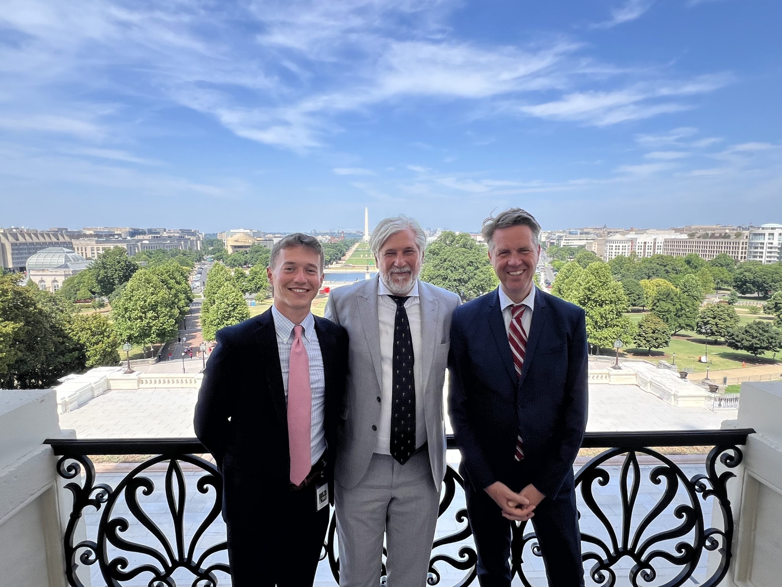 Hughes standing with two men all in suit and ties on the speaker's balcony overlooking the National Mall