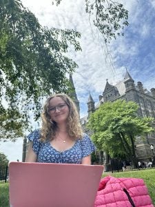 Grace on a sunny day with her laptop on the Healy Lawn