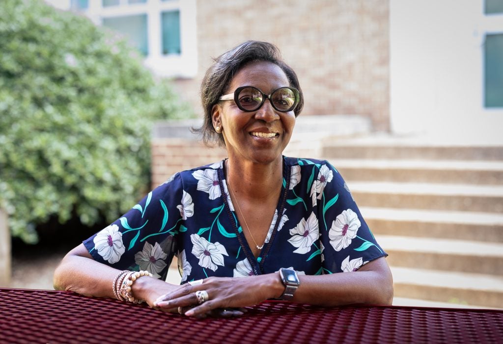 A woman with short black hair and glasses smiles over a picnic table.