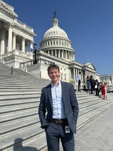 Luke Hughes in a suit standing outside of the steps of the Capitol