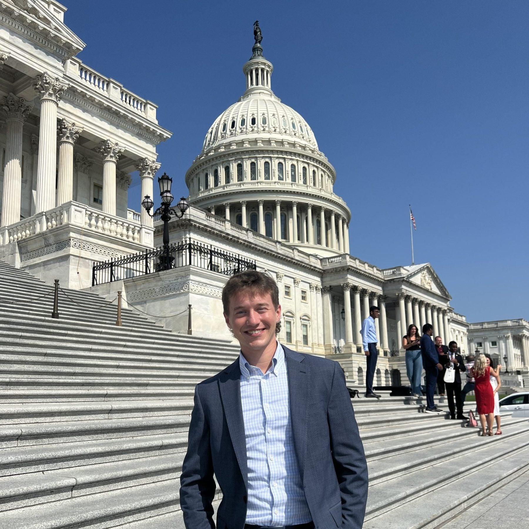 Luke Hughes in a suit standing outside of the steps of the Capitol