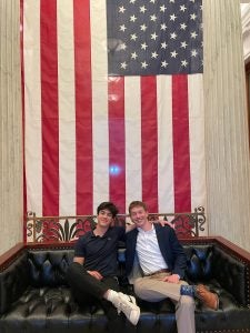 Luke Hughes with his friend Paco sitting on a couch with a US flag behind them