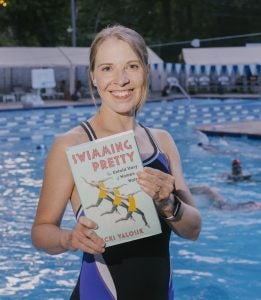 Vicki Valosik holds a copy of the book "Swimming Pretty" in front of a pool