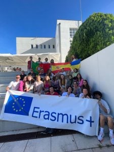 A group of international students on steps holding a banner promoting their organization Erasmus+