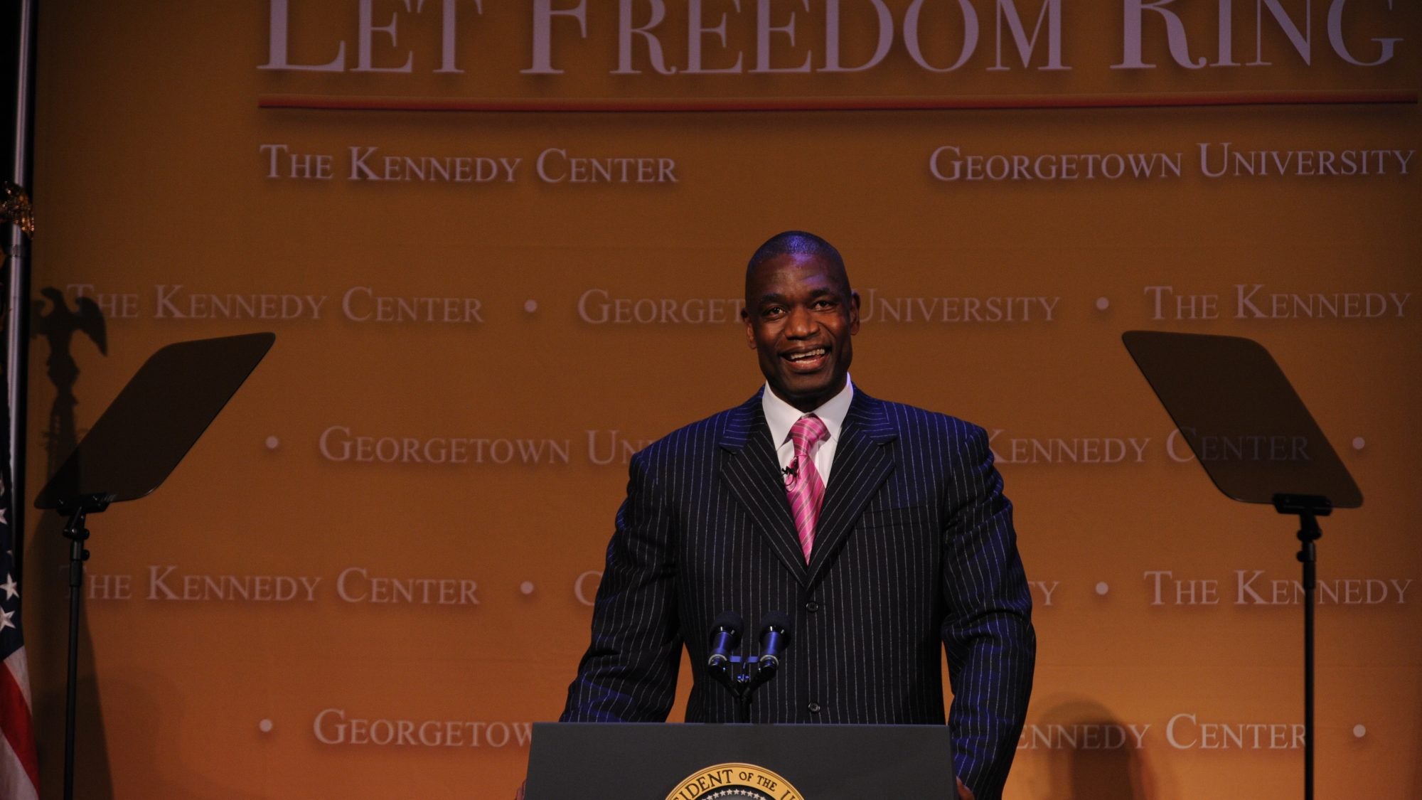 Dikembe Mutombo in front of a podium in a suit and tie