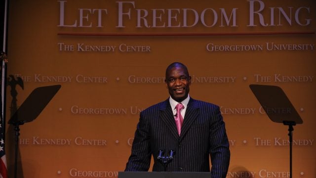 Dikembe Mutombo in front of a podium in a suit and tie